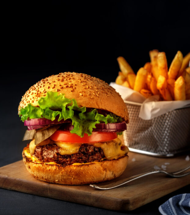 Tasty grilled beef burger with lettuce, cheese and onion served on cutting board on a black wooden table, with copyspace