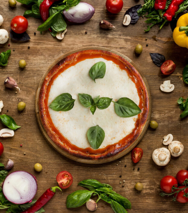 top view of pizza with fresh herbs on wooden board and various ingredients on table